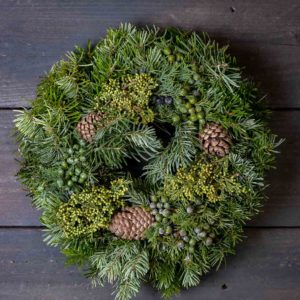 Runsas vihreä havukranssi, joka on koristeltu aidoilla kävyillä ja vihreillä marjoilla.