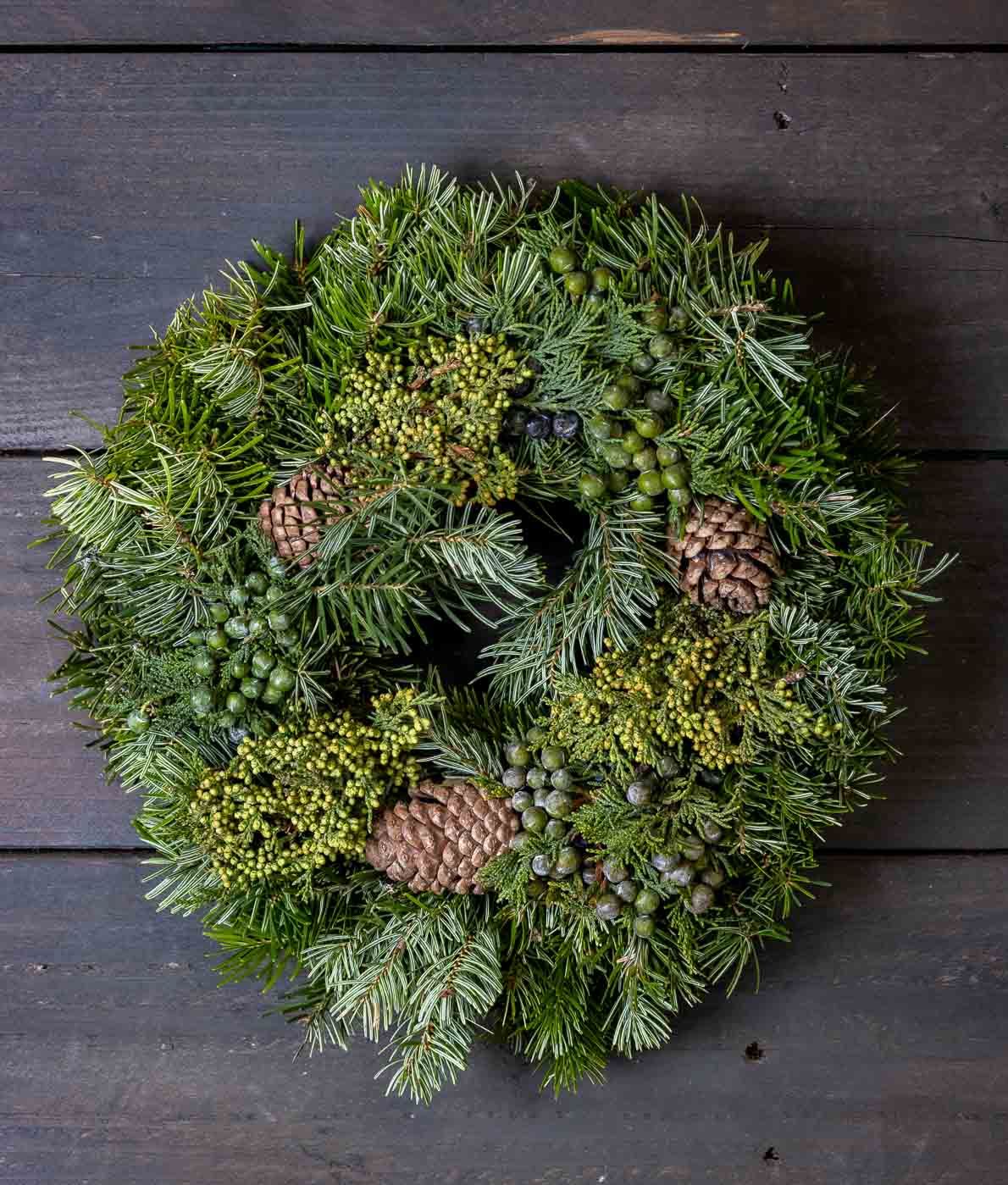 Runsas vihreä havukranssi, joka on koristeltu aidoilla kävyillä ja vihreillä marjoilla.