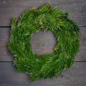 Tuuhea ja vihreä aito jalokuusikranssi kuvattuna tummaa puutaustaa vasten.