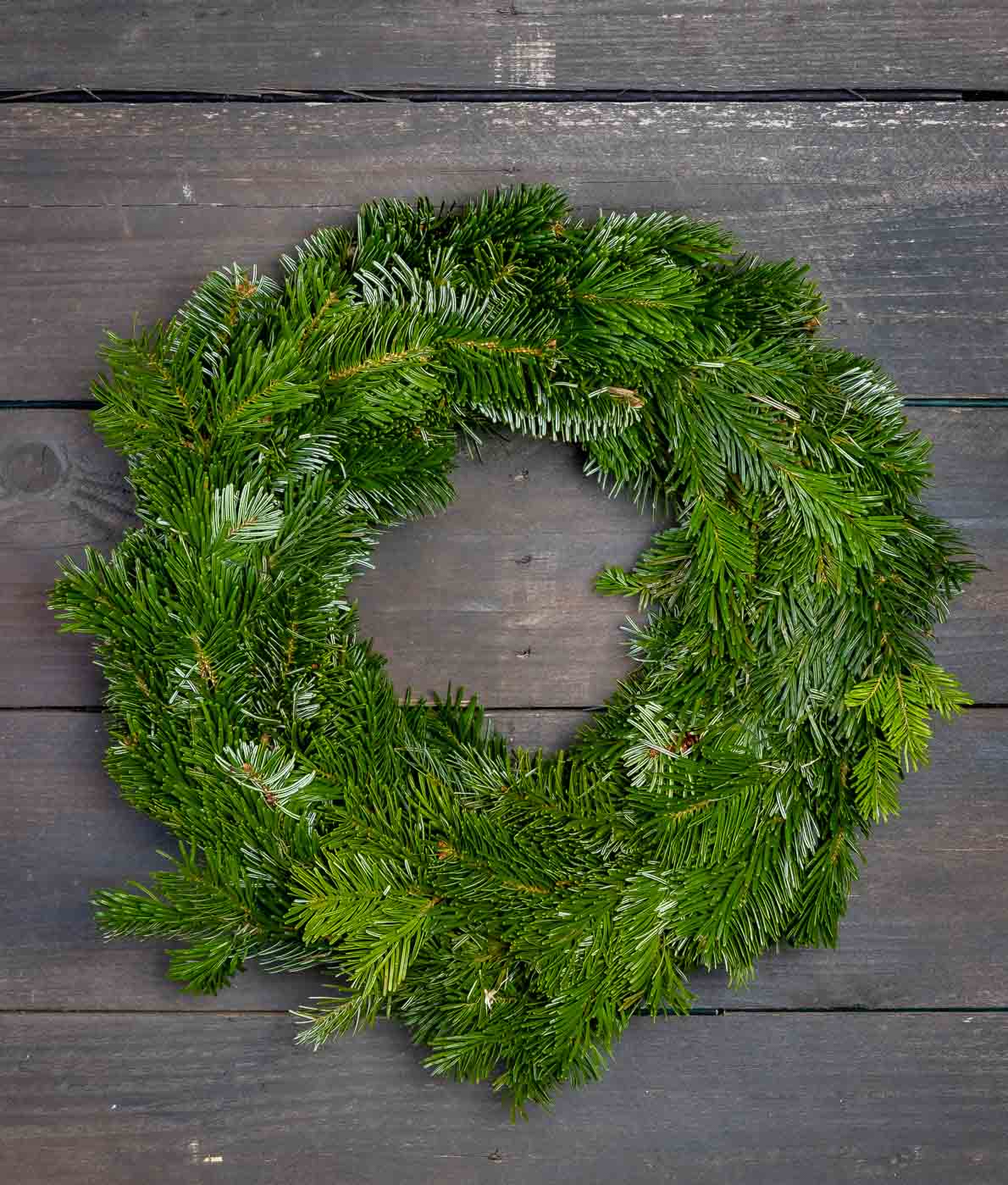 Tuuhea ja vihreä aito jalokuusikranssi kuvattuna tummaa puutaustaa vasten.