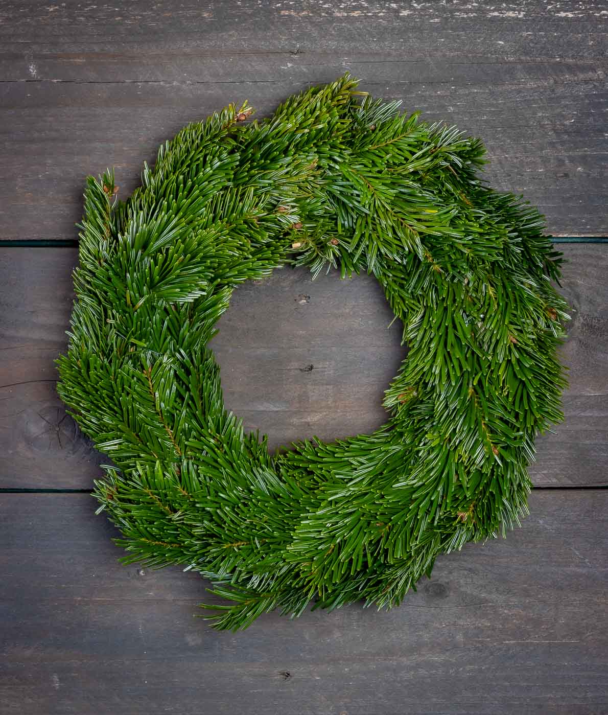 Tuuhea ja vihreä aito jalokuusikranssi kuvattuna tummaa puutaustaa vasten.