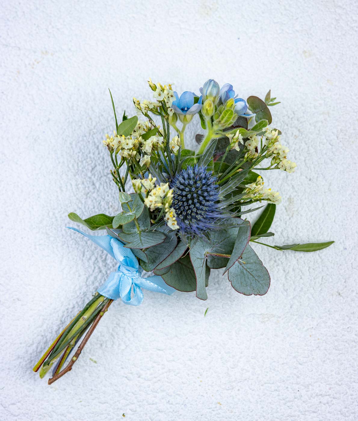 Sinisävyinen kukkaviehe piikkiputkella ja eukalyptuksella sekä sinisellä rusetilla