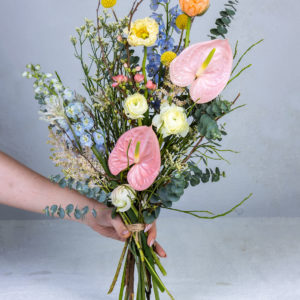 Korkea ja ilmava Talvisen Puron Juurelta -kukkakimppu, jossa on vaaleanpunaisia flamingokukkia ja sinisiä ritarinkannuksia.